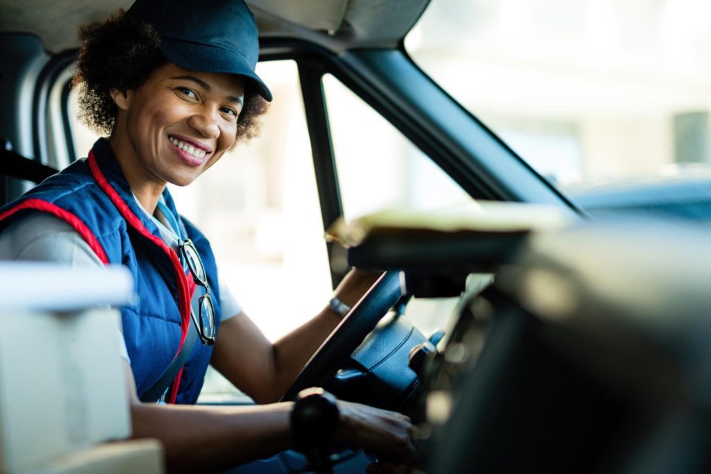 happy black female courier driving delivery van looking camera