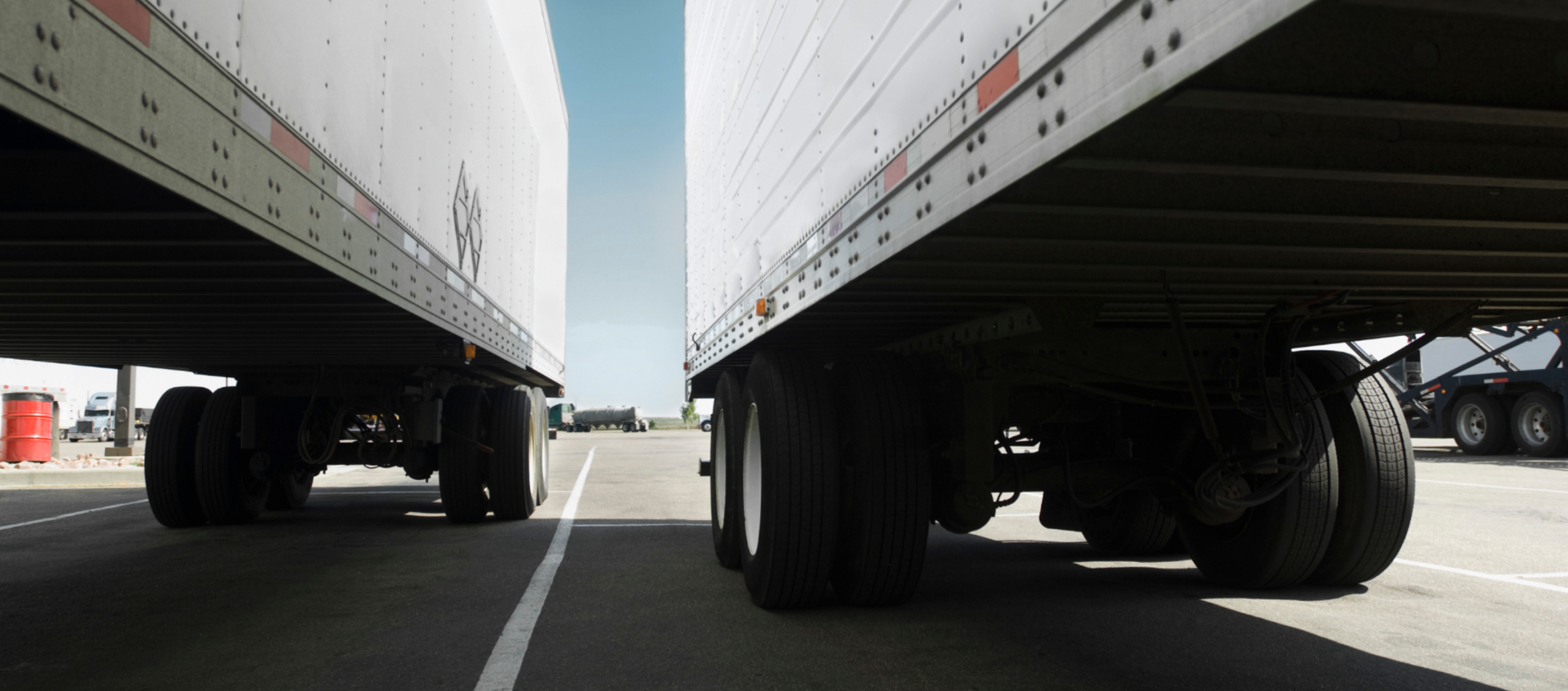 View between two semi-trailers parked at a truck stop, highlighting idle equipment during slower freight market conditions.